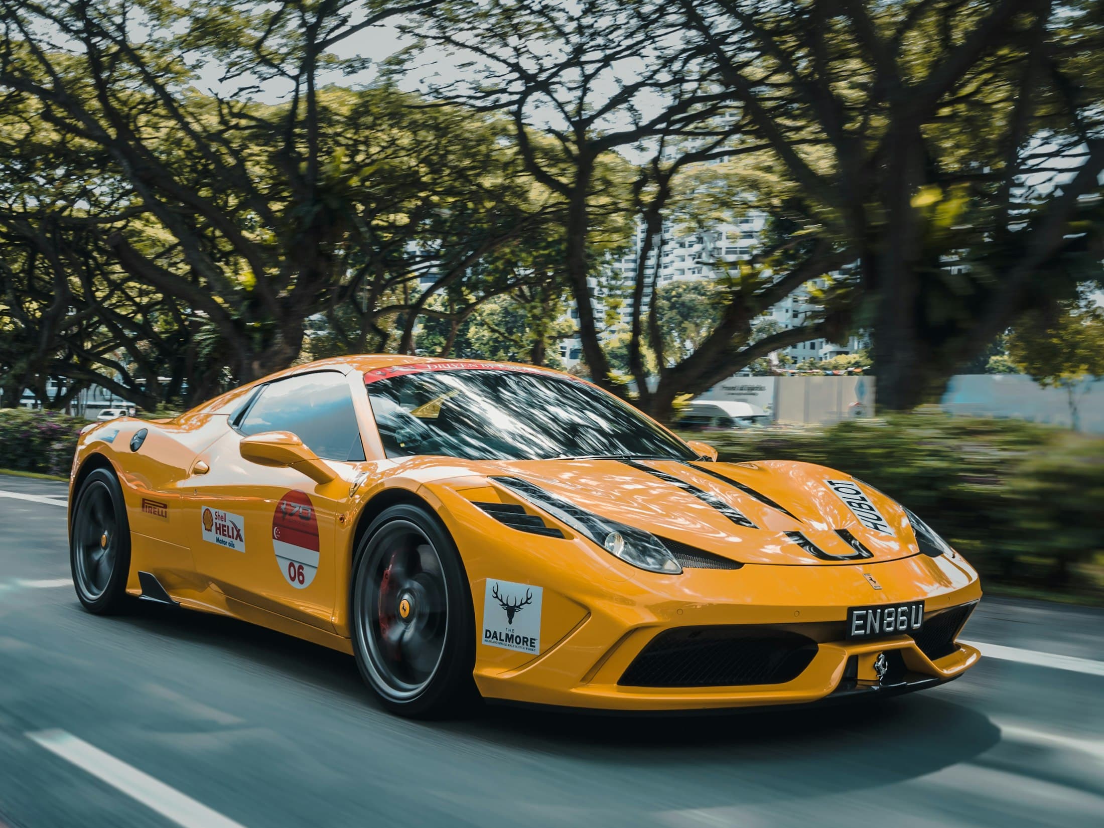Ferrari orange en livrée course sur une route bordée d'arbres