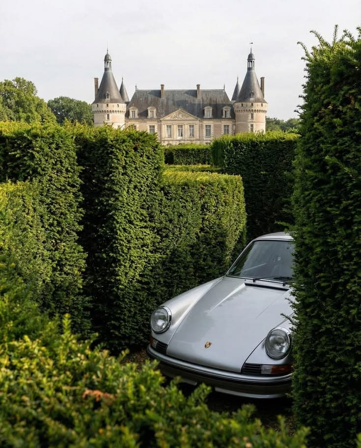 Porsche 911 grise entre des haies taillées, un château en arrière-plan